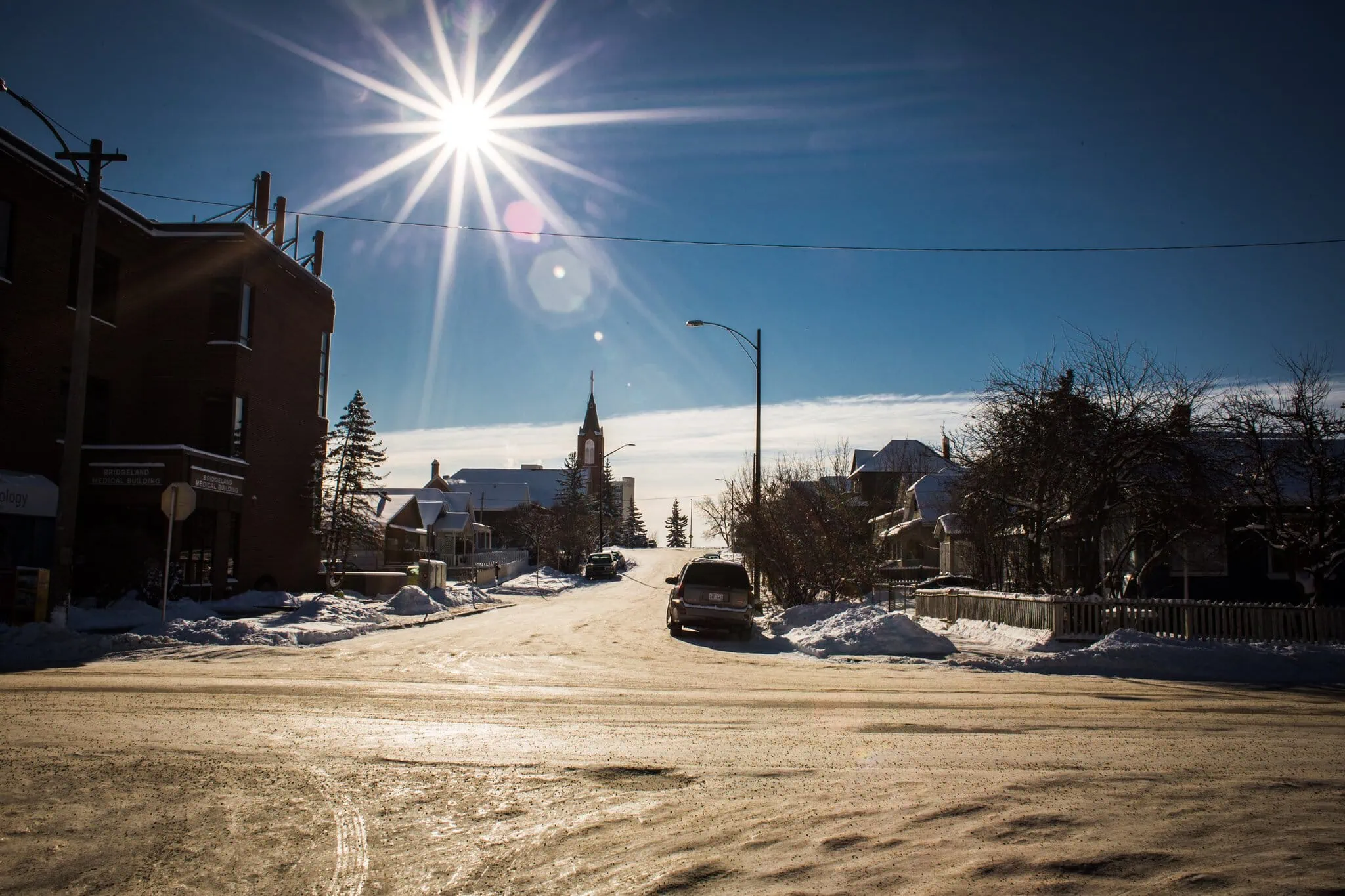 Calgary v zimě se slunečním třpytem nad zasněženou ulicí a věží kostela