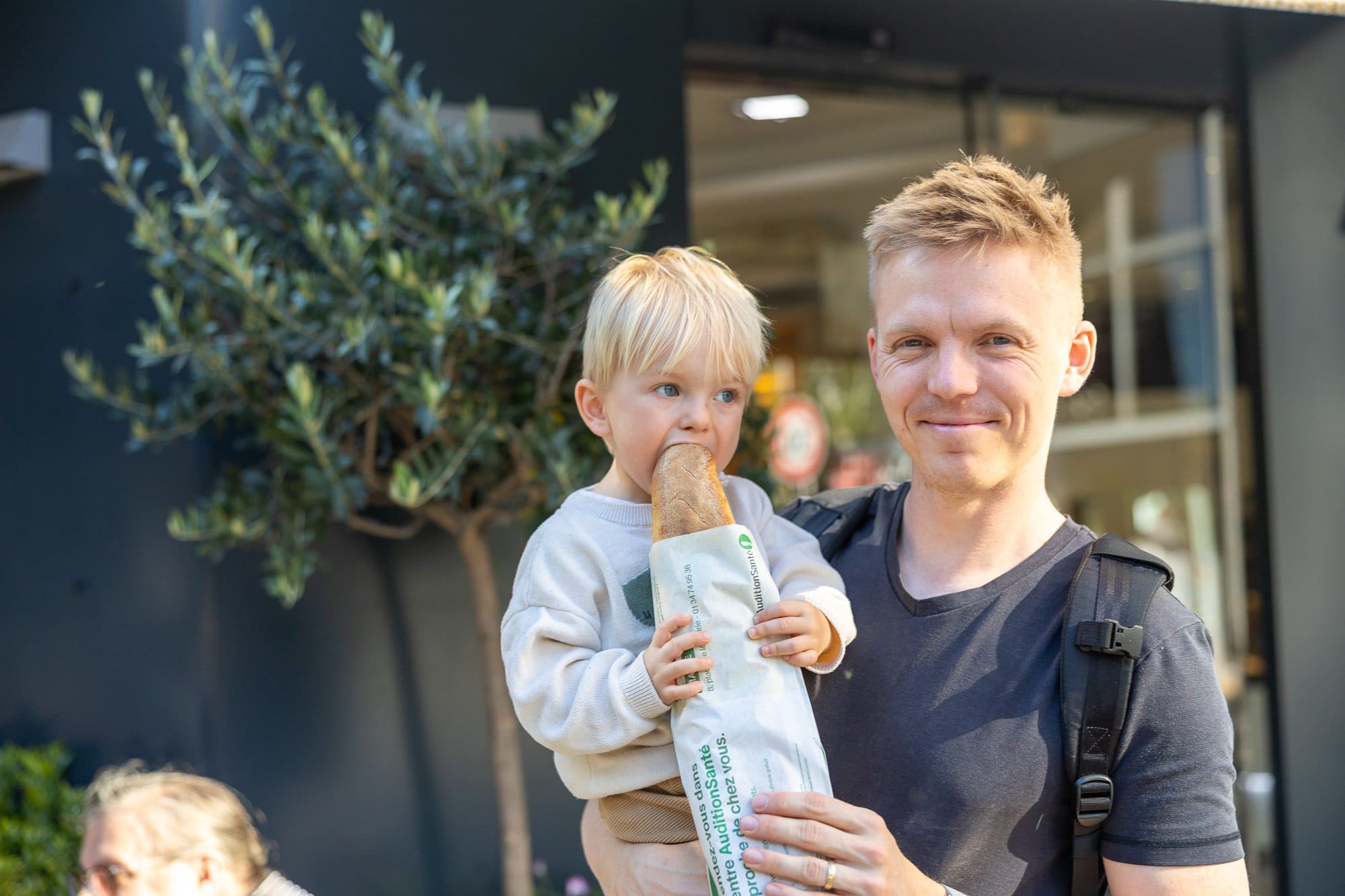 Ce să mănânci la Paris: Ghid foodie complet 2026 (bistrouri, Michelin, scena vegetariană) 5 Un tată cu fiul mic ținând o pâine în fața unui magazin din Paris