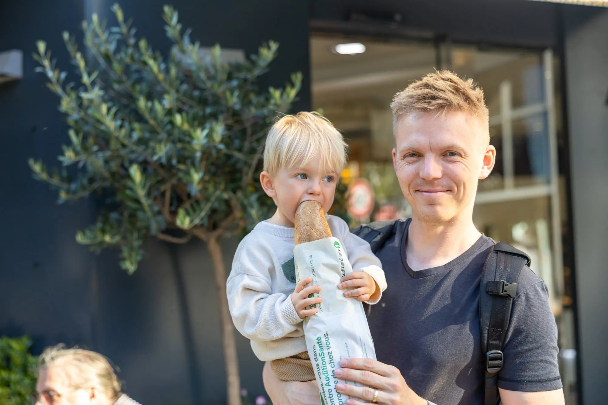 Vater mit kleinem Sohn hält ein Brot vor einem Geschäft in Paris