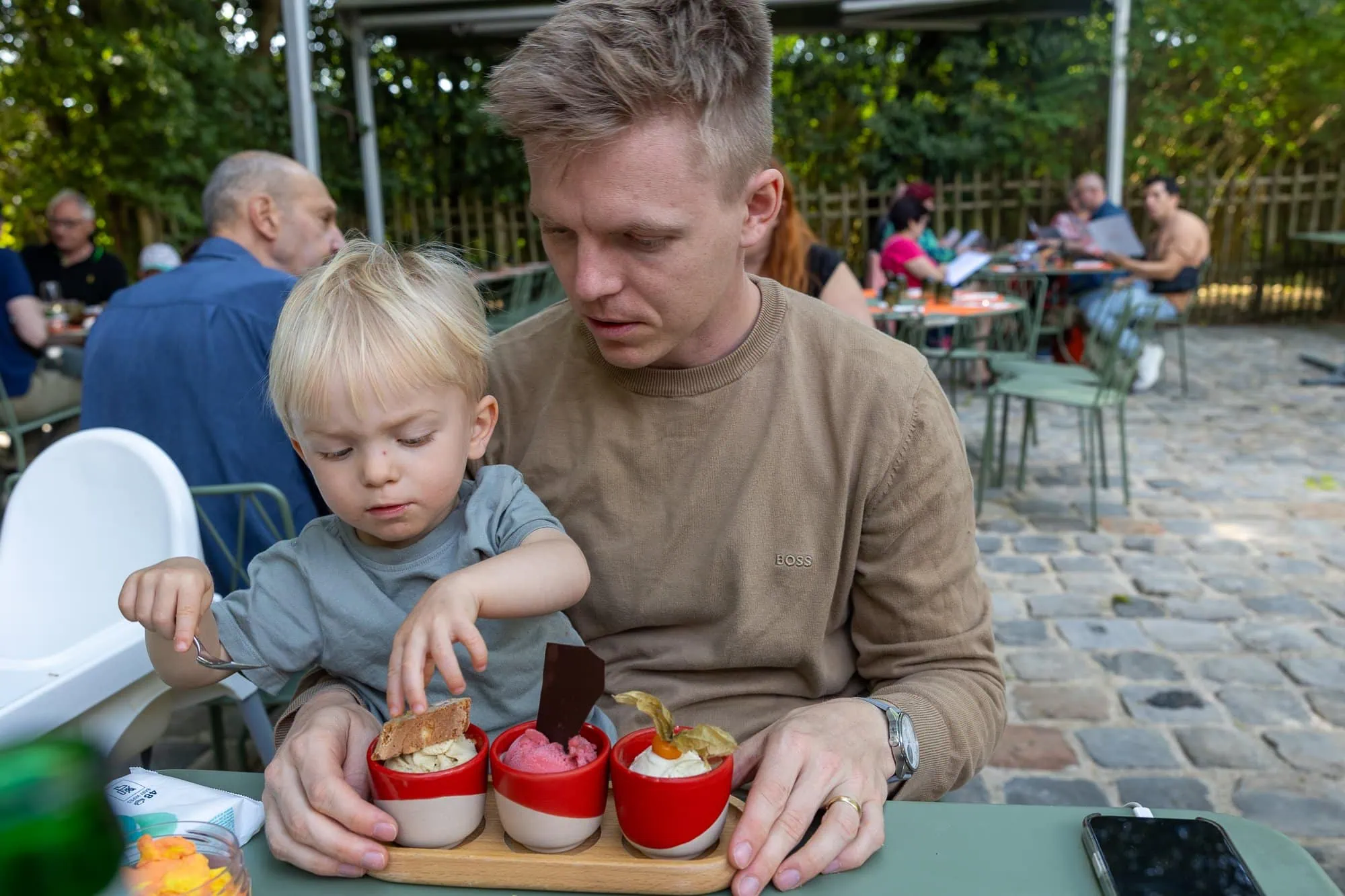 Mann und kleines Kind genießen Eis in roten Schälchen im Garten