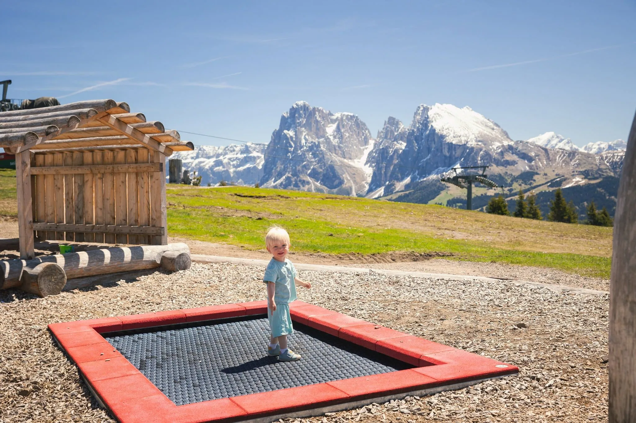 Dolomiten mit Kindern: 12 Tipps für Ausflüge (auch mit Baby) 6 Kleines Kind spielt auf einer Wiese mit Bergmassiv im Hintergrund