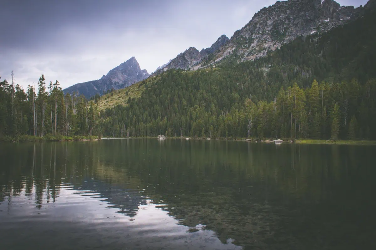 Klidne jezero s odrazem Tetonu a jehlicnatym lesem