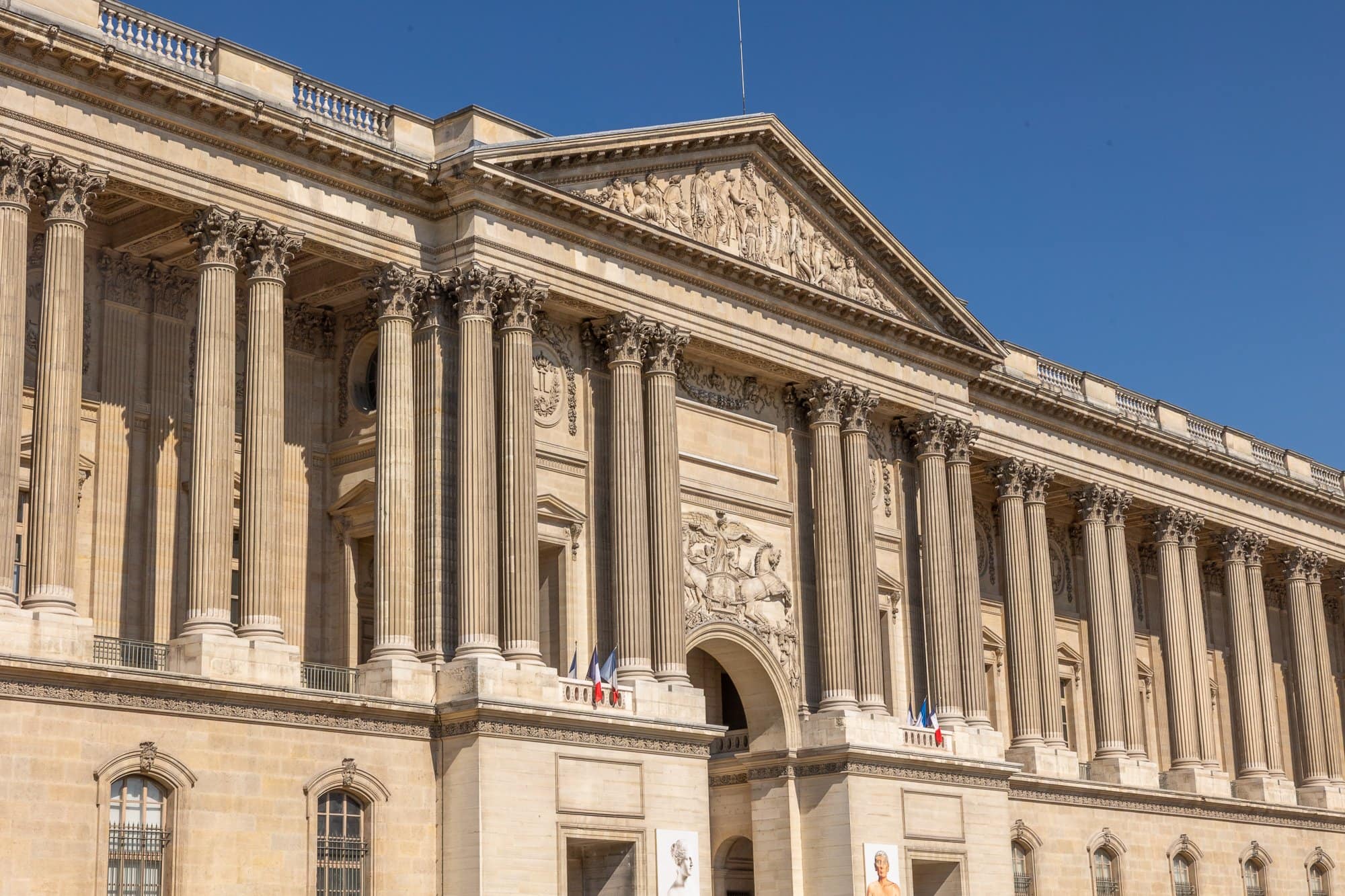 Bästa museer i Paris 2026: Från Louvren till dolda pärlor (guide till konstscenen) 1 Klassisk fasad på Louvren med joniska pelare och den franska flaggan