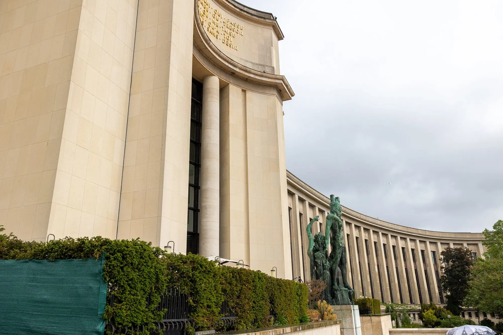 Krémovo biela klasicistická budova s radom stĺpov a sochou so zelenou patinou