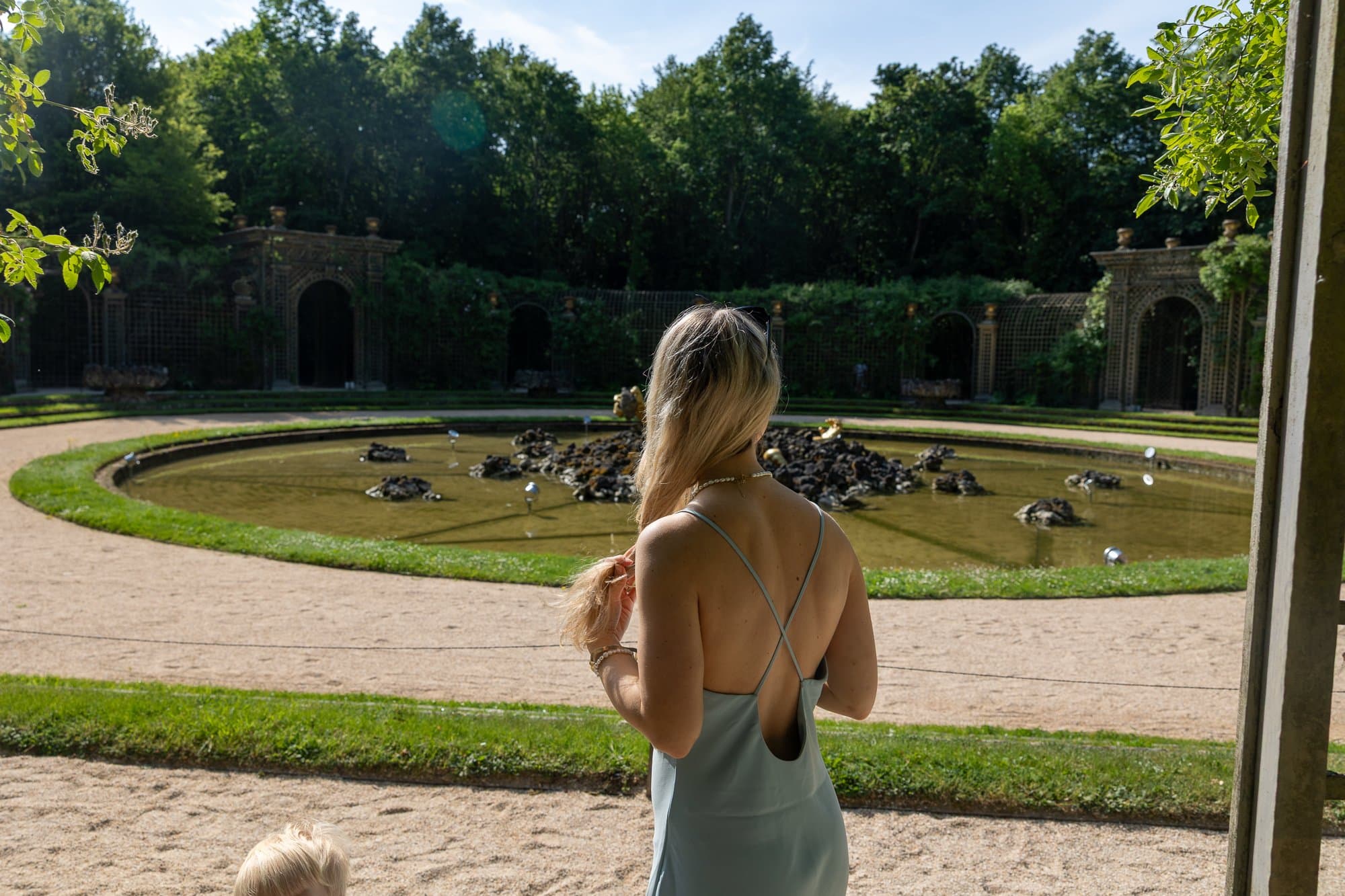 Paris cu copii: Ghidul complet pentru un city break în familie (la ce să te aștepți cu căruciorul) 15 O femeie în rochie gri privește o fântână barocă la Versailles