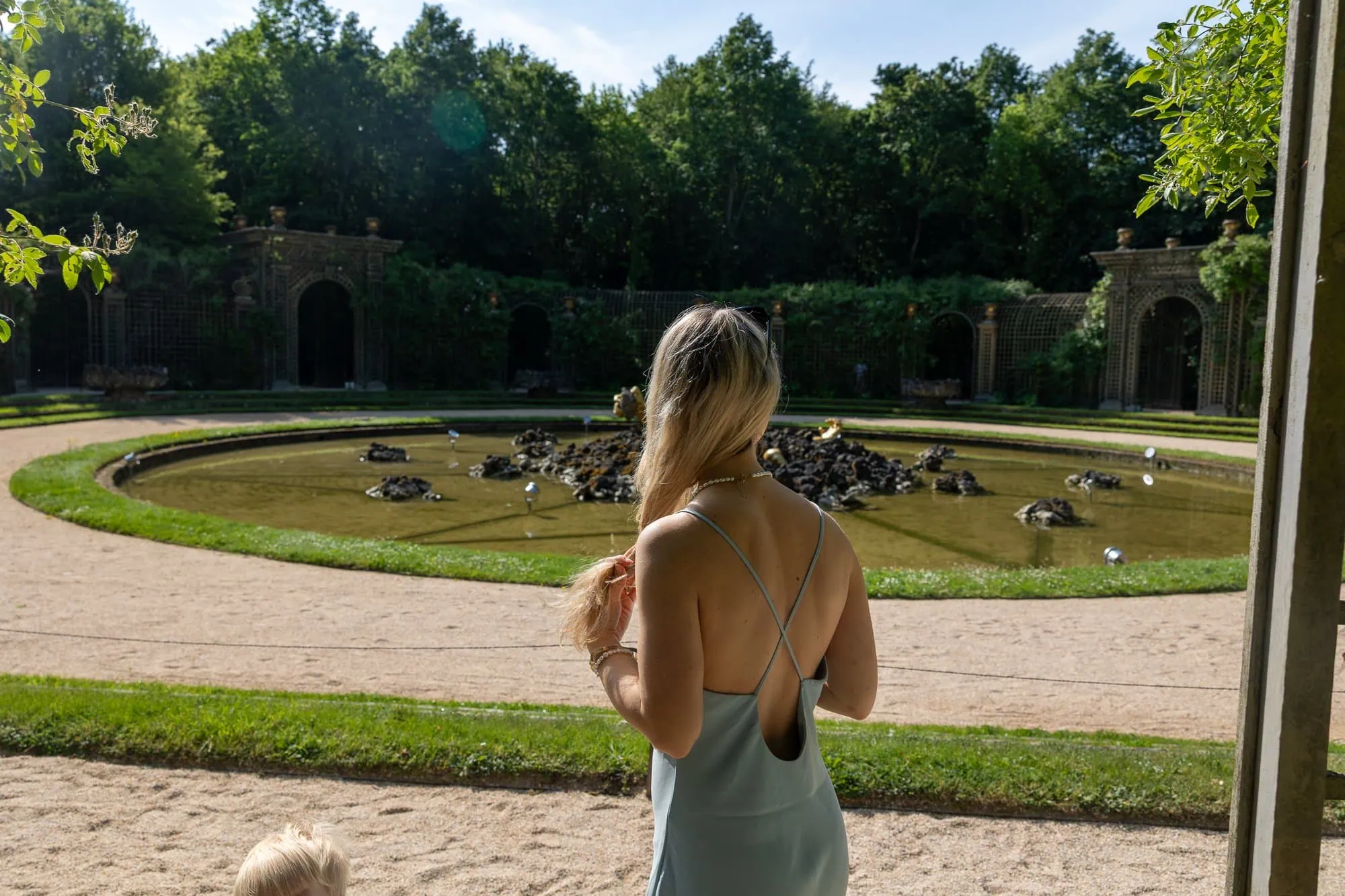 Paříž s dětmi: Kompletní průvodce rodinnou Paříží (na co se připravit s kočárkem) 14 Žena v šedých šatech kouká na barokní fontánu v Versailles
