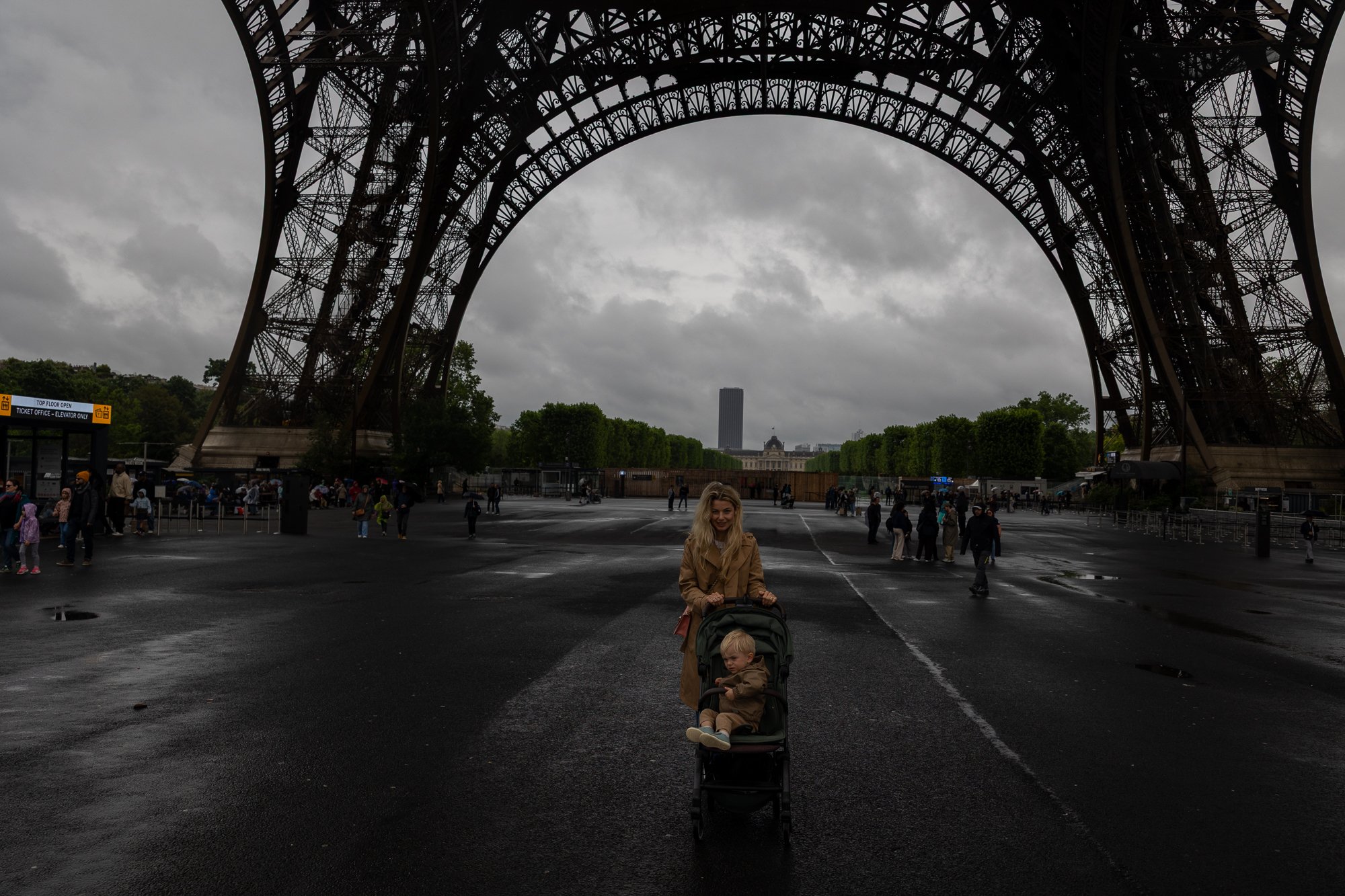 Eticheta pariziană: Cum să nu treci drept turist (dicționar, reguli, ce să NU faci) 8 O femeie cu cărucior merge sub Turnul Eiffel, cerul înnorat