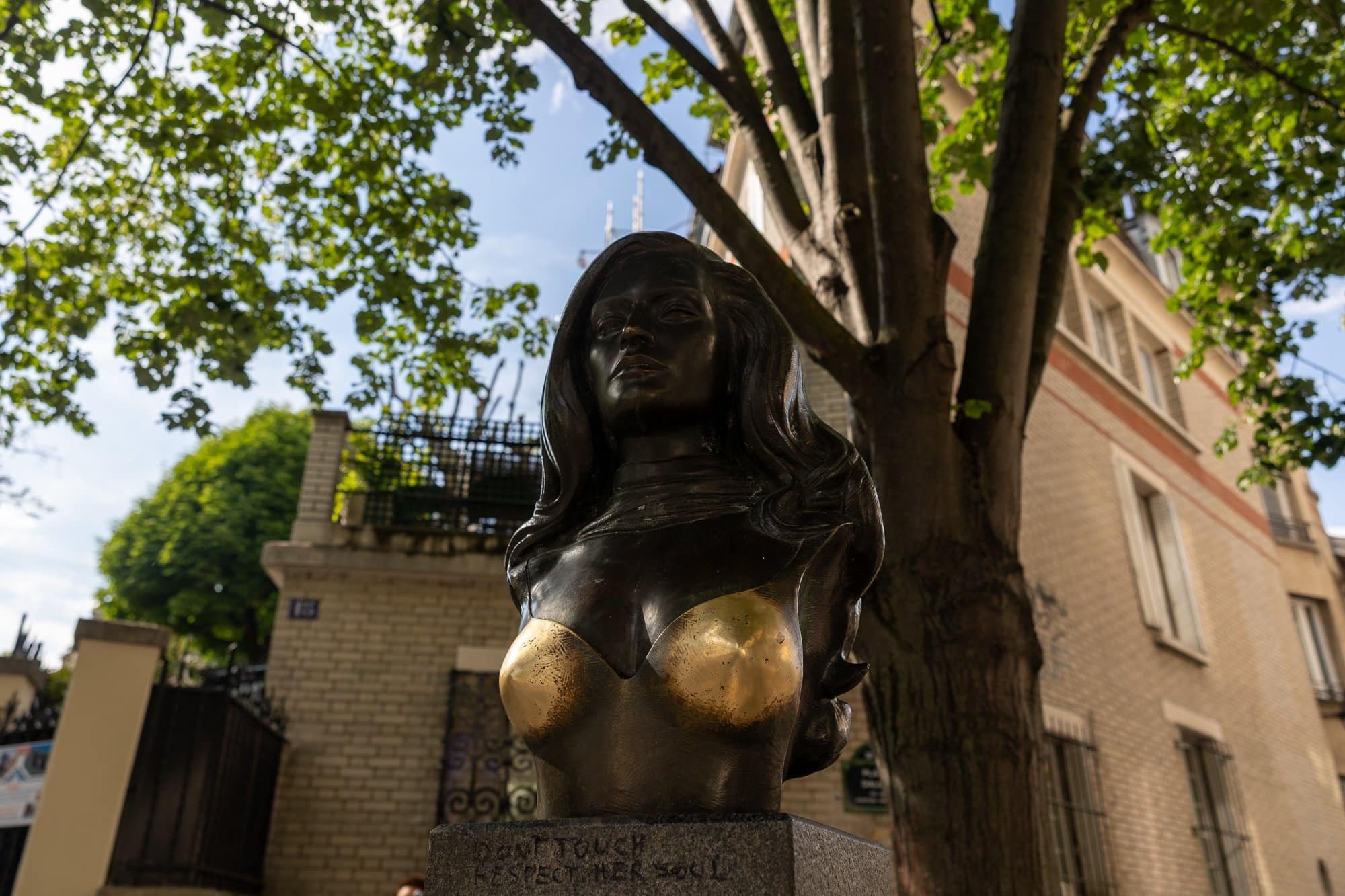 Myter och legender om Paris: Från Paris-syndromet till Fantomen på operan 7 Bronsbyst av kvinna med förgyllda detaljer på en parisisk gata under träd