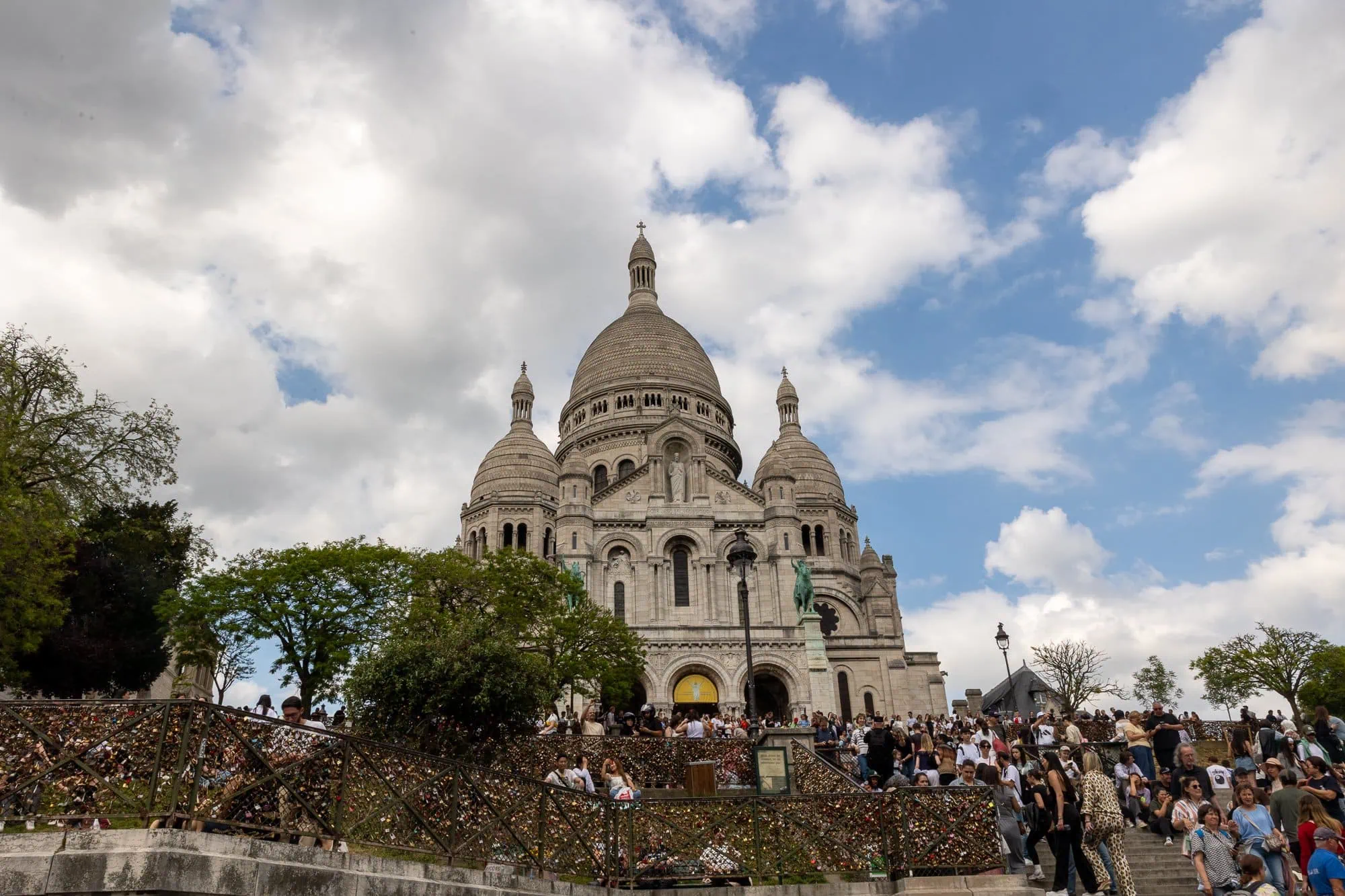 Bílá bazilika Sacré-Cœur na Montmartru s tlupy turistů a modrou oblohou