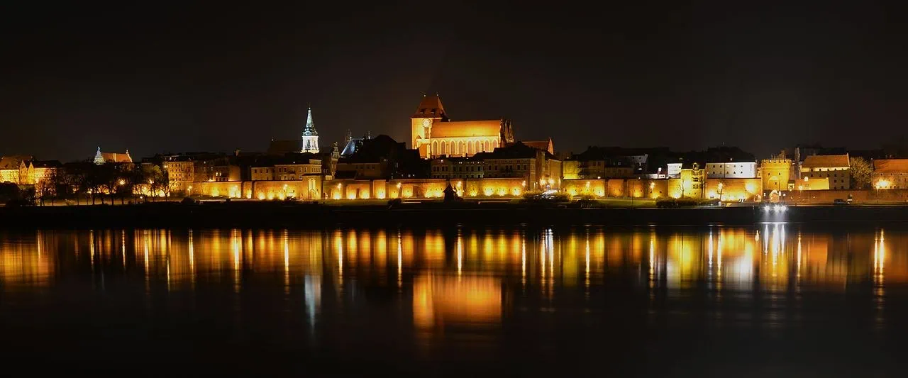 Toruň, Polsko: 12 tipů, co vidět a dělat (UNESCO, perník, Koperník) 1 Toruňské Staré Město v noci s nasvícenou siluetou kostelů a hradeb od řeky Visly