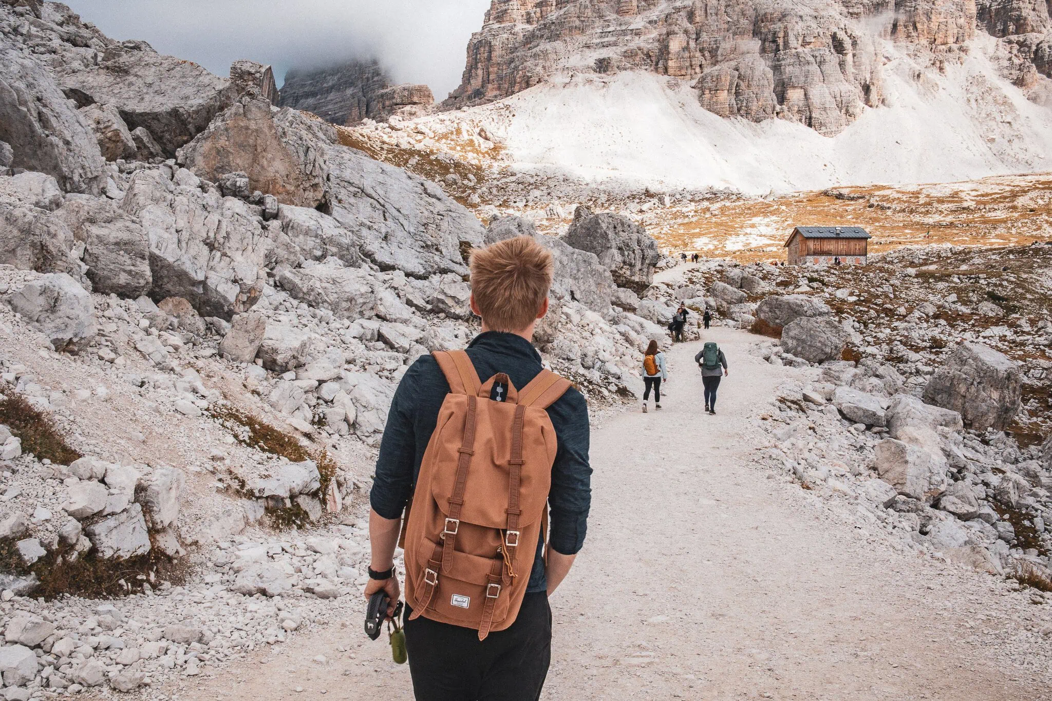 Turista s batohem na trekové stezce mezi skalními stěnami Tre Cime