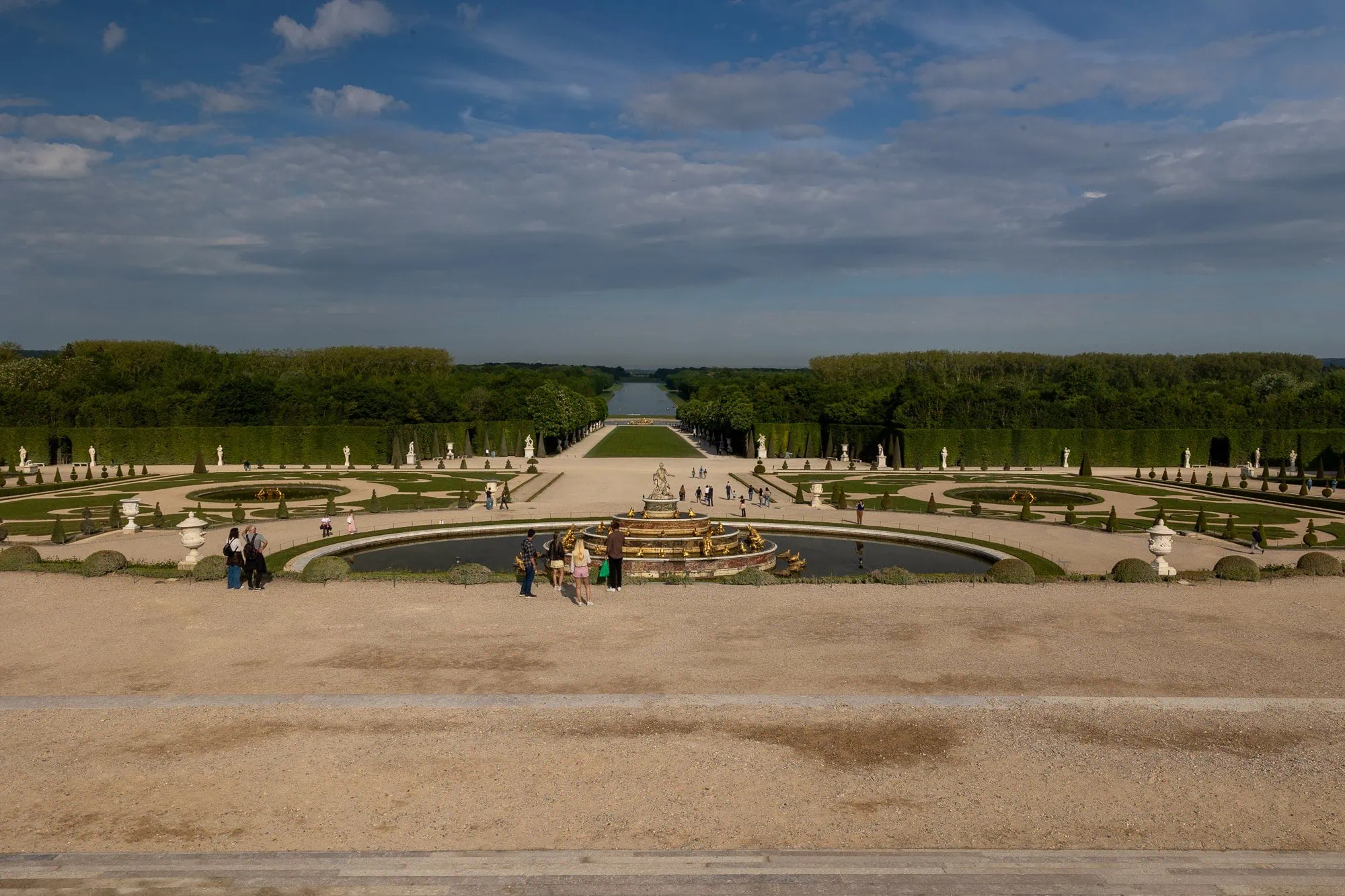 Rozlehlé formální zahrady zámku Versailles s zlatou sochou, bazénem a stromovými alejemi