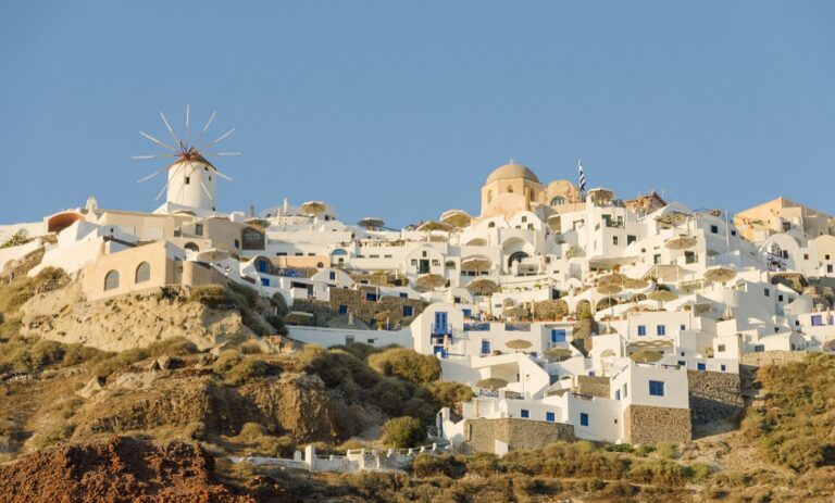 Bílé domky a modré kopule městečka Oia na Santorini nad tyrkysovým mořem