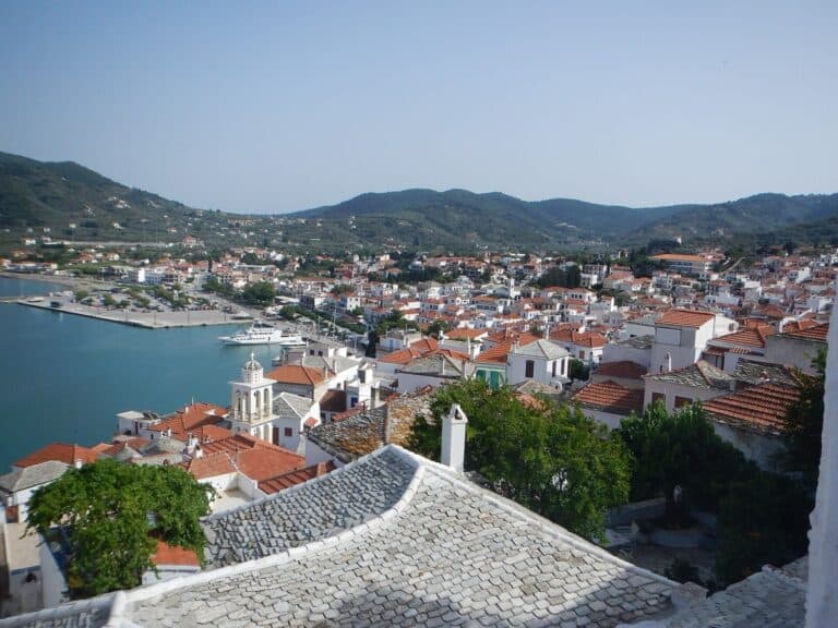 Panoramatický pohled na město a přístav Skopelos s tradiční šedou kamennou střechou v popředí, bílými domy a tyrkysovou zátokou