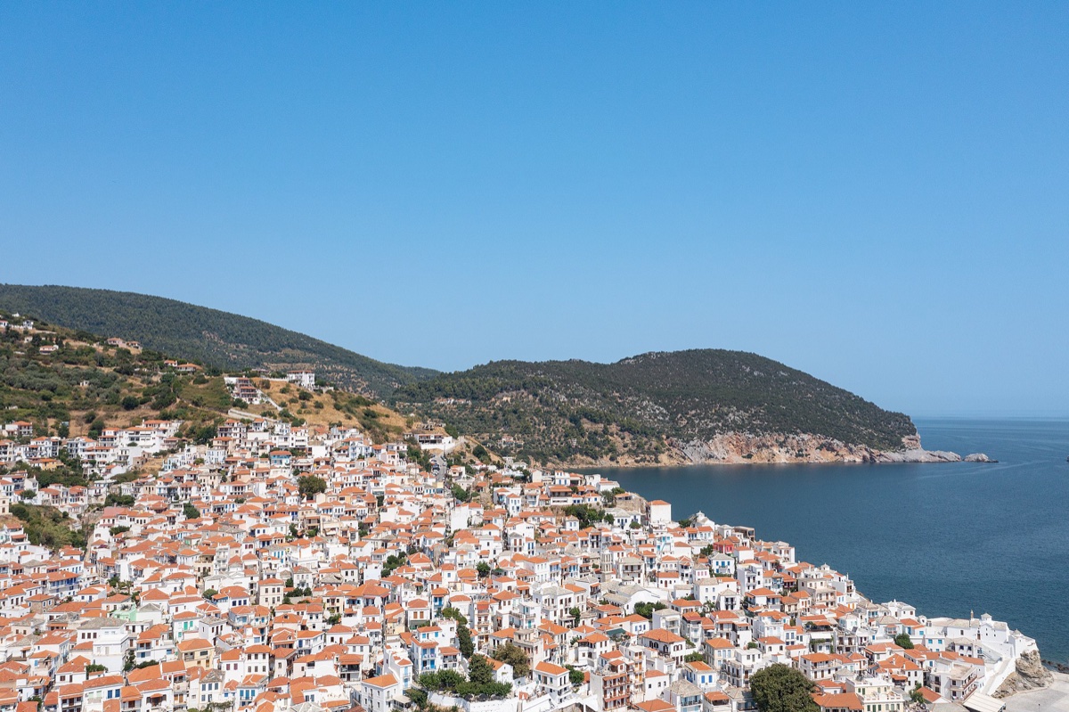 Bílé domy s terakotovými střechami města Skopelos stoupající po svahu nad mořem, tradiční egejská architektura