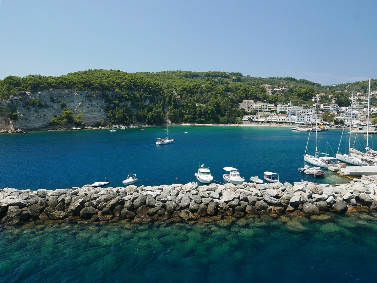 Tyrkysová zátoka přístavu Patitiri na sousedním ostrově Alonissos s jachtami, vápencovými útesy a borovicovým svahem