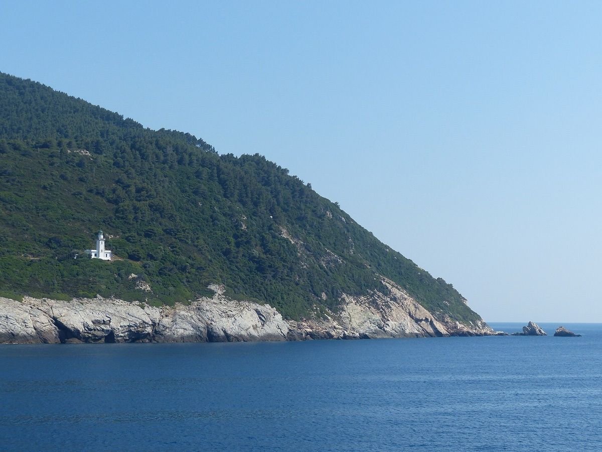 Hustě zalesněný borovicový mys ostrova Skopelos s bílým majákem nad sytě modrým Egejským mořem