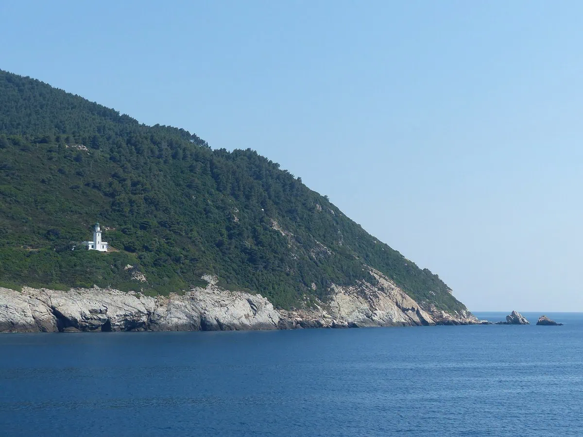 Gęsto zalesiony sosnowy cypel wyspy Skopelos z białą latarnią morską nad głęboko niebieskim Morzem Egejskim