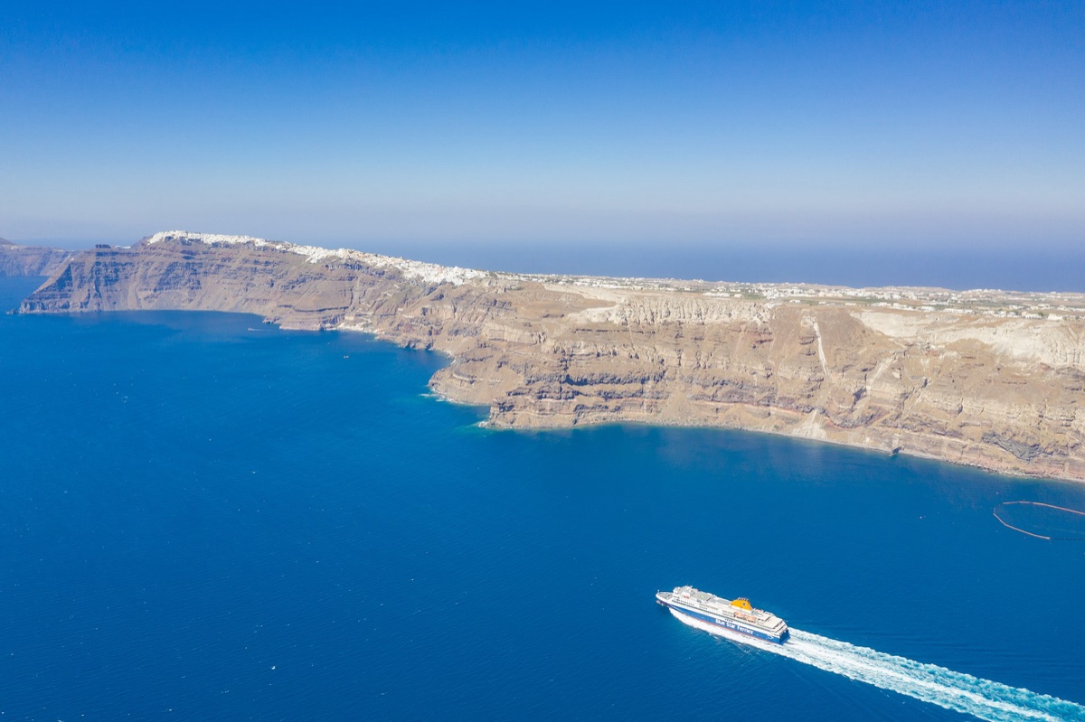 Letecký pohled na trajekt mířící k útesům ostrova Santorini v sytě modrém moři