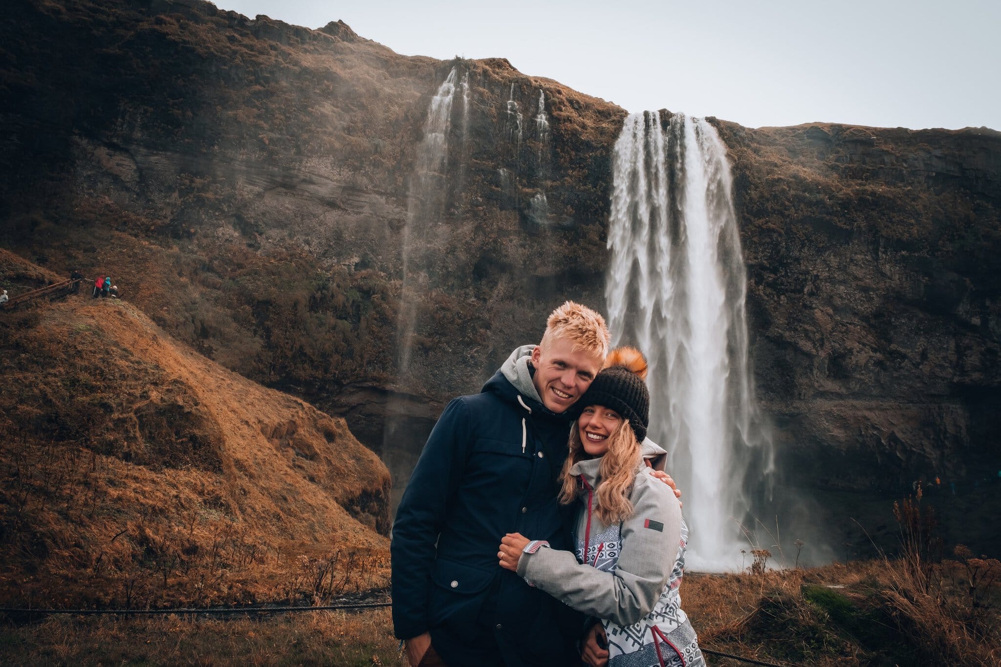 Roadtrip în Islanda: itinerariu de 14 zile + cazare 8 Un cuplu în fața cascadei înalte Seljalandsfoss în peisaj de toamnă