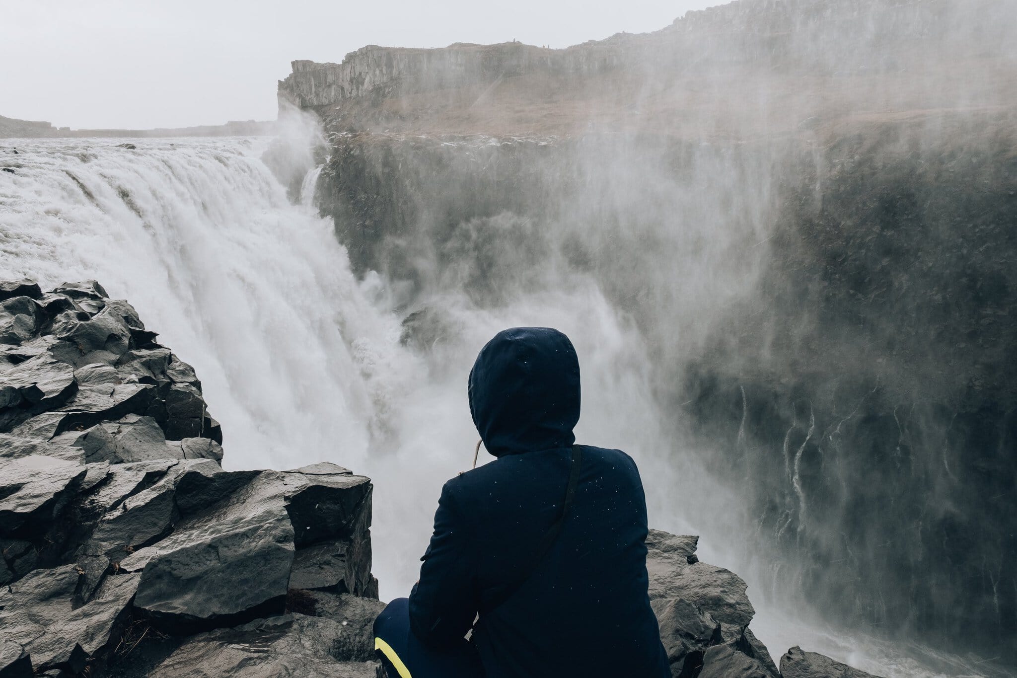 Roadtrip în Islanda: itinerariu de 14 zile + cazare 21 Un turist stă pe o stâncă lângă cascada Dettifoss din Islanda