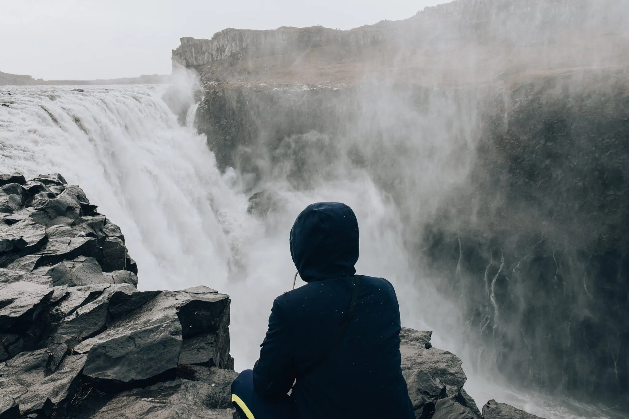 Islande du Nord et Diamond Circle : 12 choses à voir et à faire en 2026 15 Un touriste assis sur un rocher près de la cascade Dettifoss en Islande