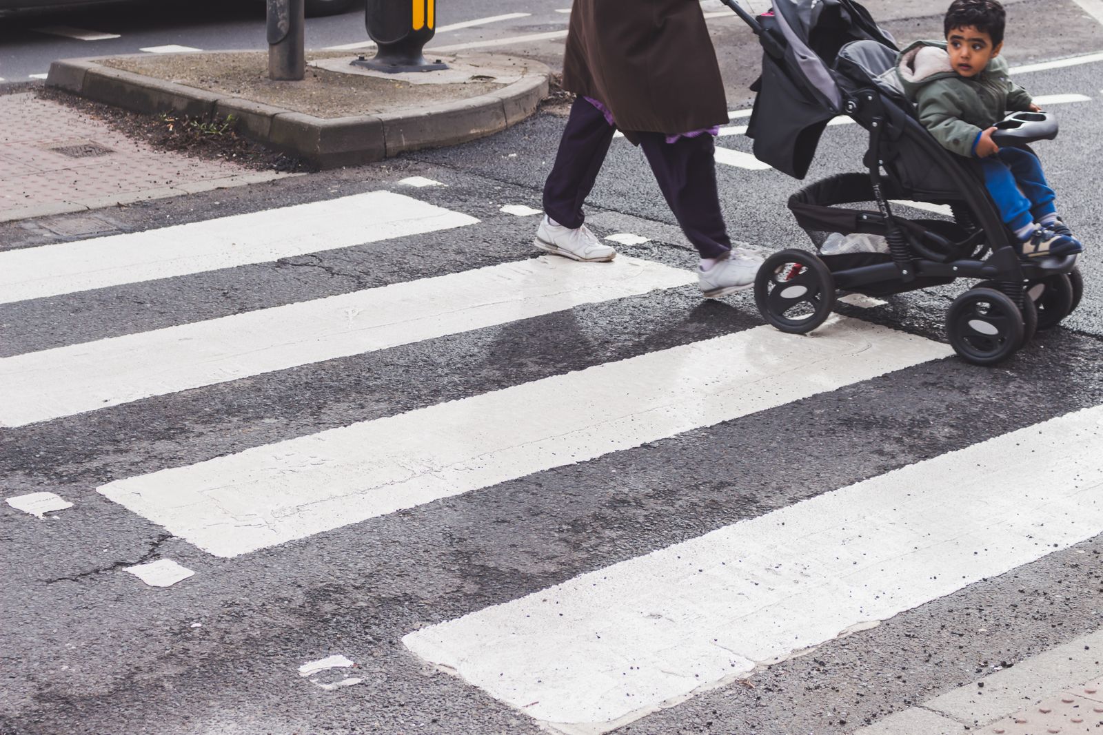 Passeggino in aereo: cosa passa gratis e cosa no nel 2026 1 Un genitore con un bambino nel passeggino attraversa le strisce pedonali