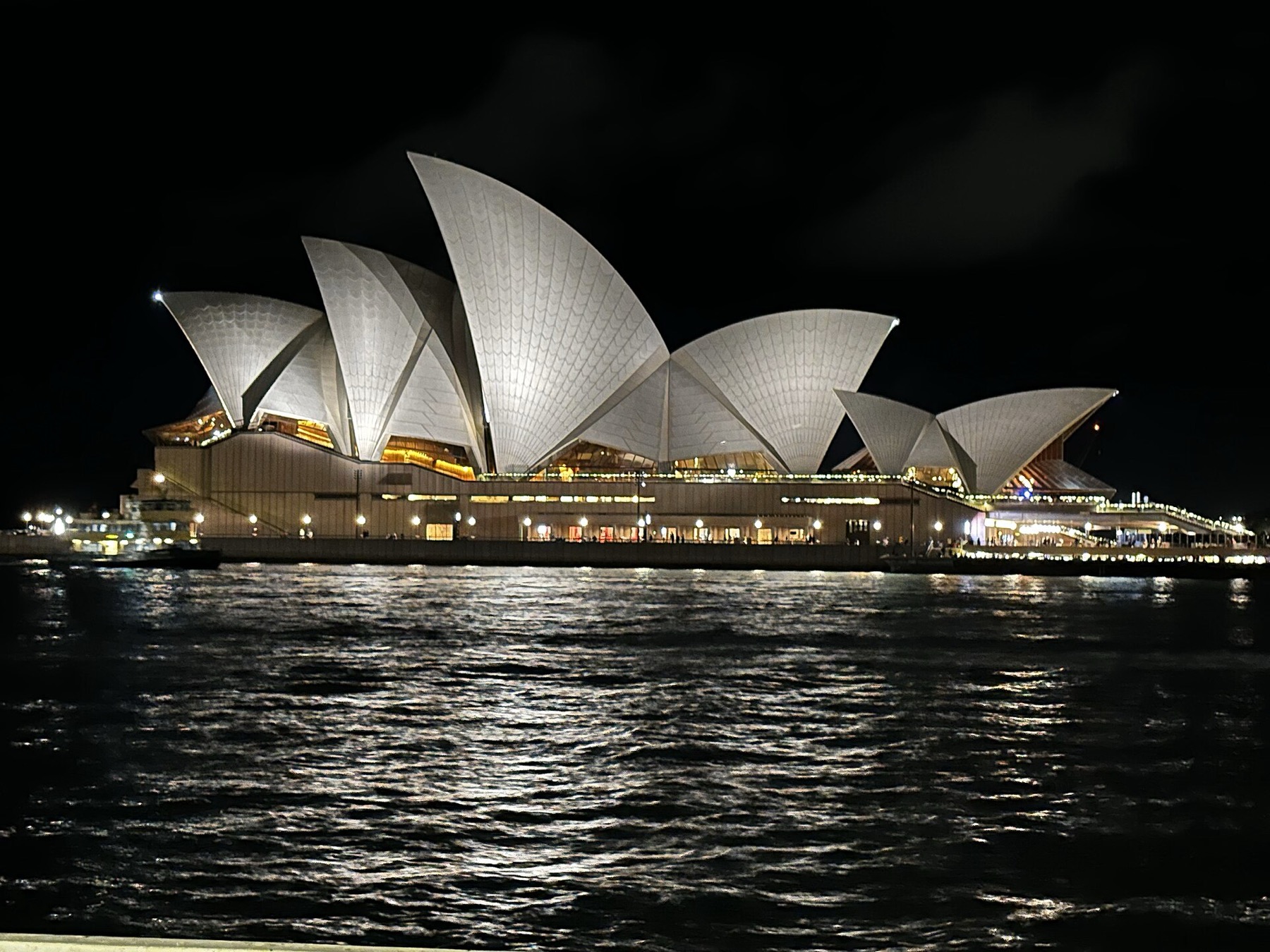 Sydney operaház Ausztráliában: jegyek, túrák és minden, amit 2026-ban tudnod kell 6 Az operaház kivilágított vitorlái sötétedés után, a Badu Gili vetítés hátterében